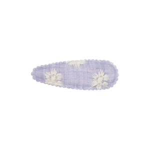 Détail d'une pince à cheveux en tissu lavande brodé de trois motifs floraux sur fond blanc pur