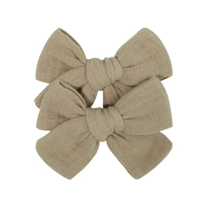 Close-up of two oatmeal linen bow hair clips with textured fabric for babies