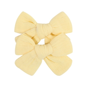 Macro detail of two light yellow handcrafted fabric bow hair clips for infants