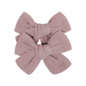 Detail view of two fabric bow hair clips in soft dusty pink with textured cotton gauze