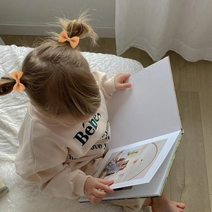 Détail de barrettes à nœuds en ruban gros-grain abricot portées par un bébé qui lit