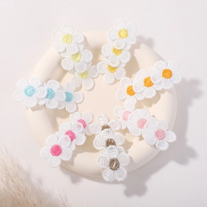 Détail de six barrettes à fleurs de marguerites brodées colorées sur un plateau blanc
