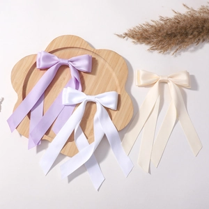 Gros plan de trois nœuds à cheveux en satin violet, blanc et beige sur plateau bois
