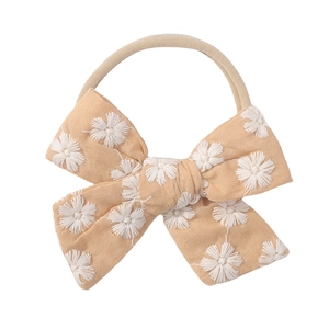 Detail of baby bow headband featuring white daisy embroidery on soft beige linen fabric