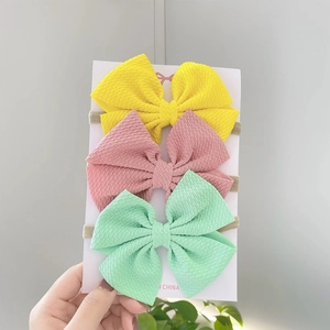 Detailed view of three textured waffle fabric bow headbands in yellow, pink and green