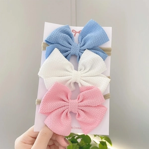 Three-piece set of textured baby bow headbands in blue, white, and pink on display card