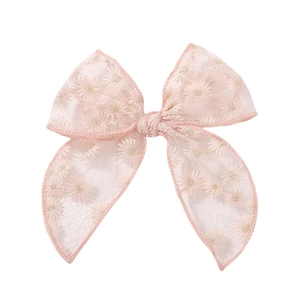 Détail de nœud à cheveux en maille rose avec broderie de marguerites et texture en dentelle