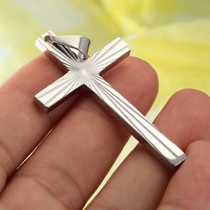 Silver stainless steel cross necklace with radial sunburst texture held in hand