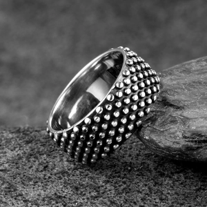 Herren-Ring aus Edelstahl im Punk-Stil mit Metallnieten auf einem dunklen Steinhintergrund