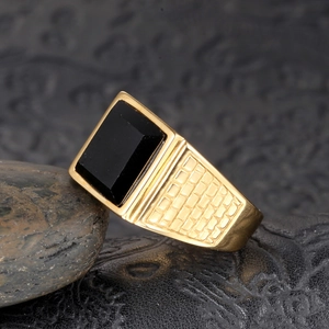 Vue macro d'une bague pour homme en acier doré avec pierre noire et anneau à texture grillée
