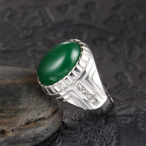 Vista macro de anillo para hombre con gema verde ovalada y banda plateada con diamantes