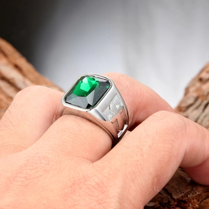 Detail of men's titanium steel ring with green emerald gemstone and cross relief