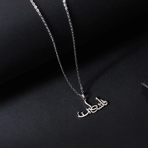 Collier en acier inoxydable argenté avec écriture arabe sur fond sombre texturé