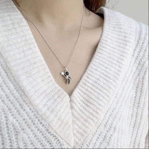 Close-up of a silver astronaut pendant necklace with a star on a white knitted sweater