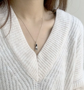 Close-up of a silver astronaut pendant necklace with a star detail on a knit sweater