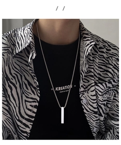 Polished silver cylinder pendant necklace on model with black and zebra pattern clothing