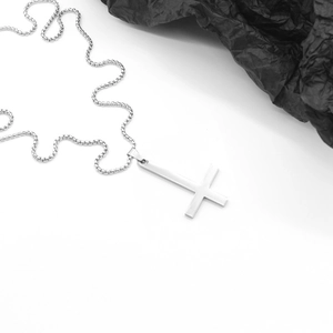 Pendentif croix inversée en acier poli avec chaîne box sur fond texturé noir élégant