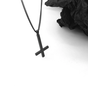 Gros plan d'un pendentif croix inversée noir mat avec une fine chaîne à maillons noirs