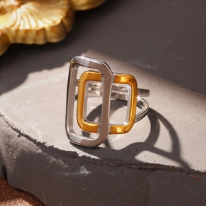 Macro shot of interlocking silver and gold rectangular rings on a textured stone base