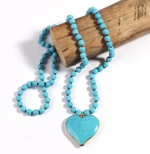 Detail of bohemian turquoise heart pendant necklace with gold trim on rustic wood