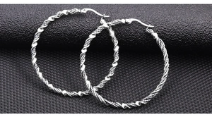 Gros plan de boucles d'oreilles créoles torsadées argentées à la texture métallique
