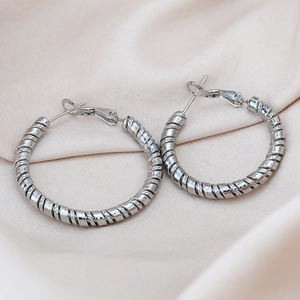 Détail macro de boucles d'oreilles créoles torsadées argentées sur de la soie beige