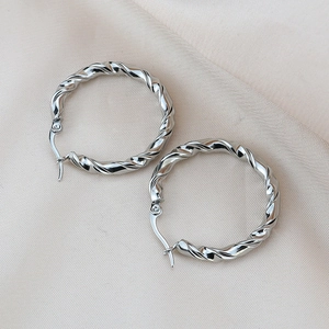 Détail de boucles d'oreilles créoles torsadées argentées sur un fond en tissu beige
