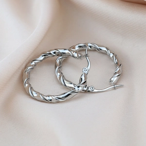 Détail macro de boucles d'oreilles créoles torsadées argentées sur tissu de soie