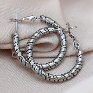 Détail d'une boucle d'oreille créole argentée avec une texture en spirale torsadée