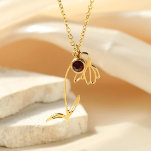 Detail of gold flower pendant necklace featuring a ruby-red zircon on a stone background