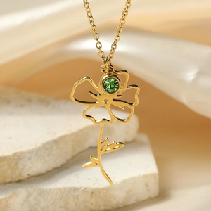 Detailed close-up of golden floral pendant with green crystal on elegant stone background
