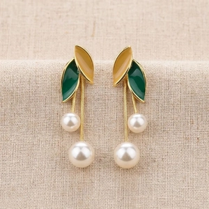 Elegant leaf earrings with tassels and faux pearls on natural linen texture