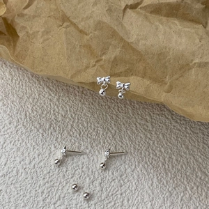 Detail of S925 sterling silver bow knot earrings with polished silver beads on a textured surface