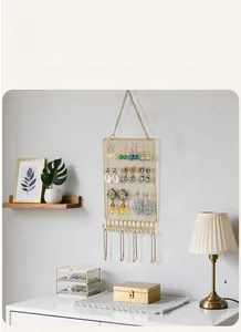 Detail view of gold metal wall-mounted jewelry organizer with grid and hanging hooks