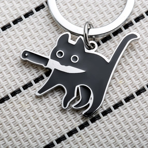 Close-up of a humorous black cat with knife enamel keychain on a woven texture background