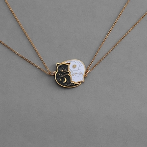 Matching cat pendant necklaces in gold with black and white enamel sun moon yin yang design
