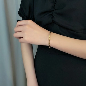 Bracelet jonc ouvert doré en forme de bambou porté par un mannequin en robe noire