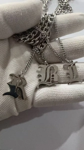 Gros plan des pendentifs lettres gothiques R, B et L en acier titane sur une chaîne