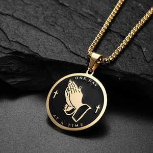 Golden stainless steel necklace with praying hands pendant on black rock background