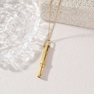 Detail of a gold whistle necklace with ribbed texture on white stone and glass background