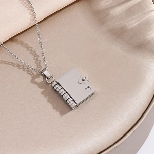Polished stainless steel book locket necklace with hollow heart detail on silk background