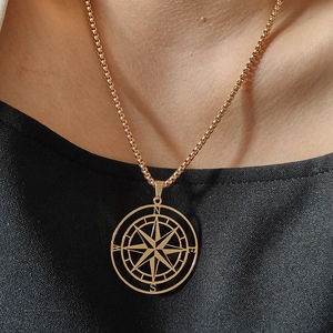 Star compass pendant necklace in gold finish worn by model on a black textured background