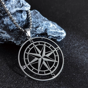 Macro shot of a silver compass pendant necklace with N E S W engraving on a rock