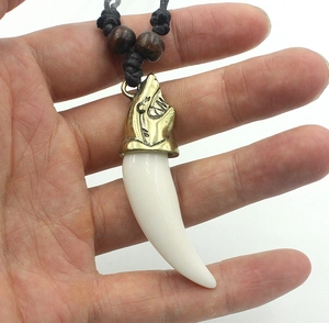 Close-up of wolf tooth resin pendant with bronze wolf head and black braided cord