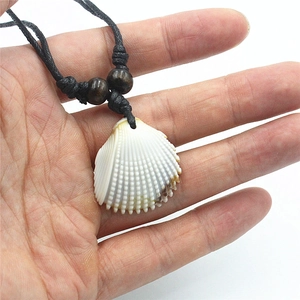 Vue à la main d'un collier pendentif coquillage blanc avec cordon noir et perles