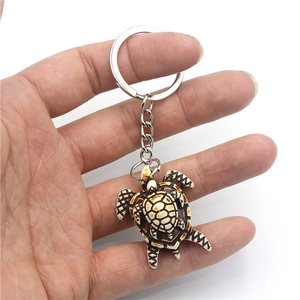 Porte-clés tortue en résine avec bébé tortue tenu à la main sur fond blanc neutre