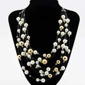 Detail showing multi-layer beaded necklace with white pearls and gold accents on a black bust