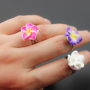 Detailed view of handmade clay flower rings featuring pink and purple frangipani on hand