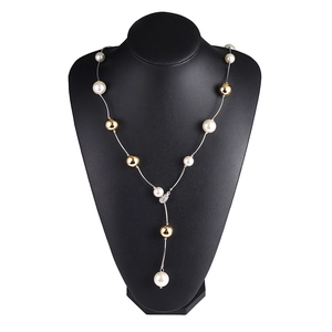 Long collier en Y avec perles blanches et accents dorés sur un buste de bijoux noir