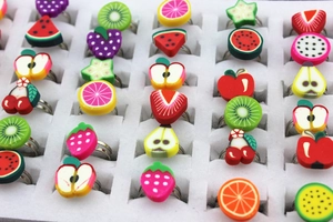 Close-up of children's adjustable fruit rings with colorful clay designs in a white display box